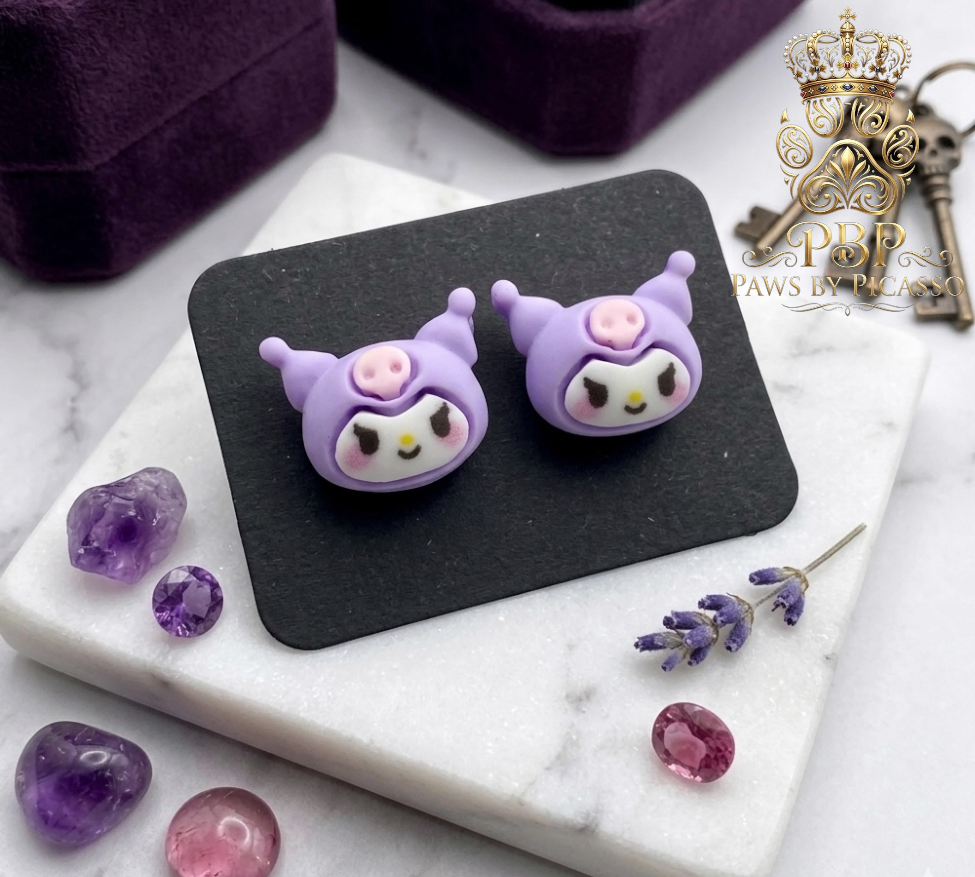 Purple cartoon-themed earrings on a black stand with decorative stones on a marble surface.