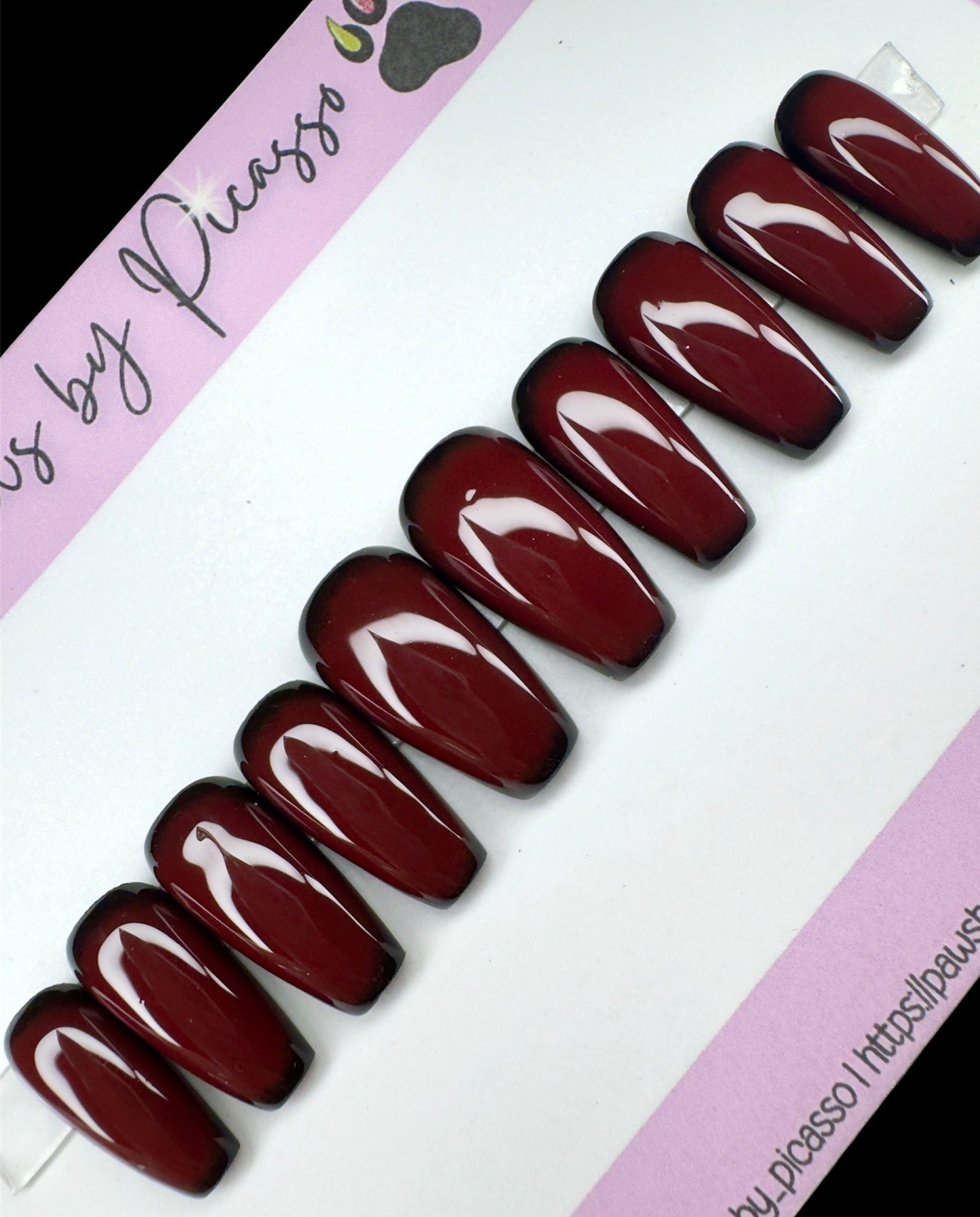 Set of dark red nails on a white and pink background with 'Paws by Picasso' branding.