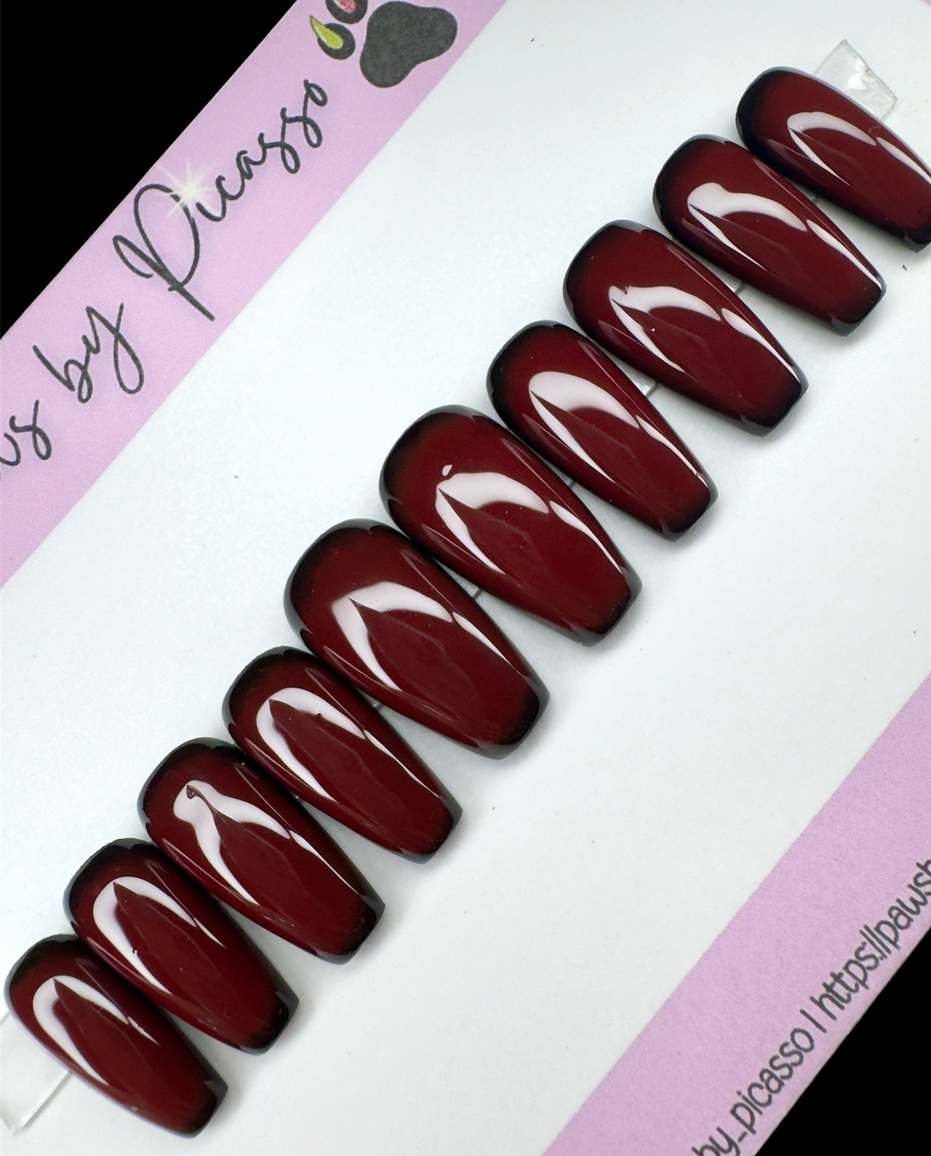 Set of dark red nails on a white and pink background with 'Paws by Picasso' branding.