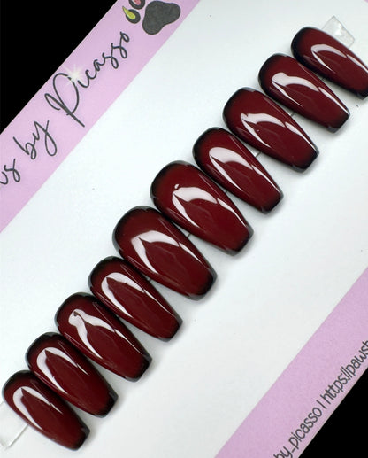 Set of dark red nails on a white and pink background with 'Paws by Picasso' branding.
