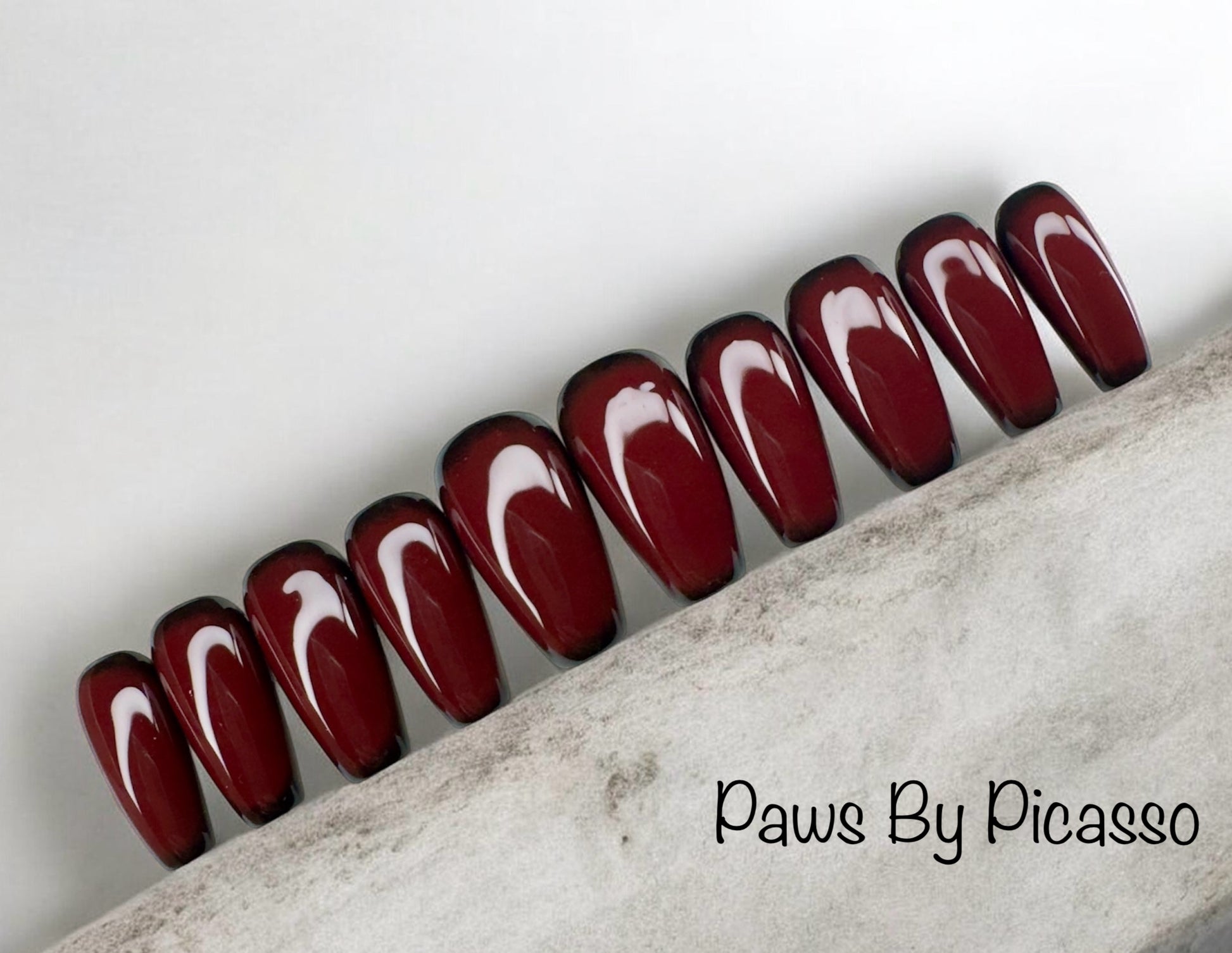 Row of red and black false nails on a textured surface with 'Paws By Picasso' branding.