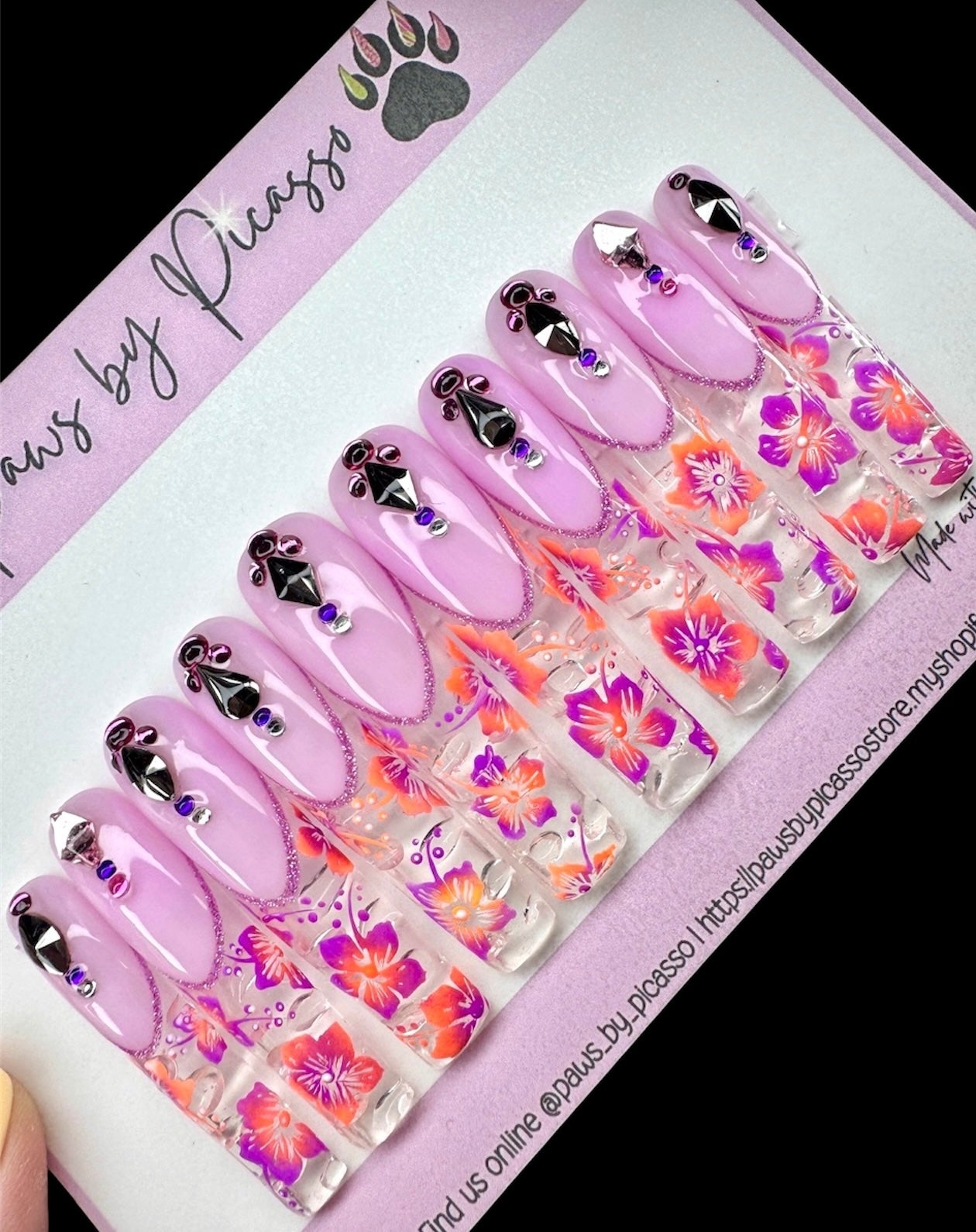 Set of purple nail art designs with floral patterns on a branded packaging.