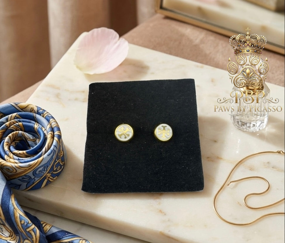Gold earrings on a black display card with a decorative ribbon and perfume bottle in the background.