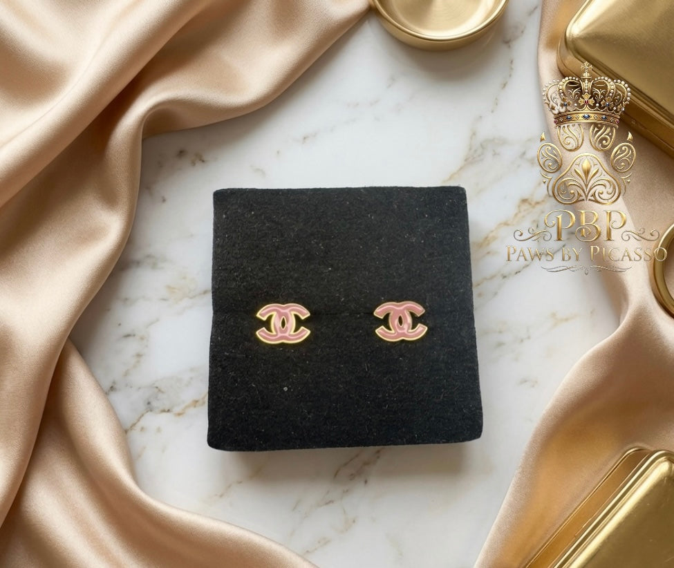 Pair of gold earrings on a black square pad with a marble background and 'Paws by Picasso' logo.