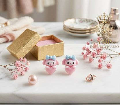 Pink animal-shaped earrings with a gold box and flowers on a marble surface, featuring the brand 'Paws By Picasso 