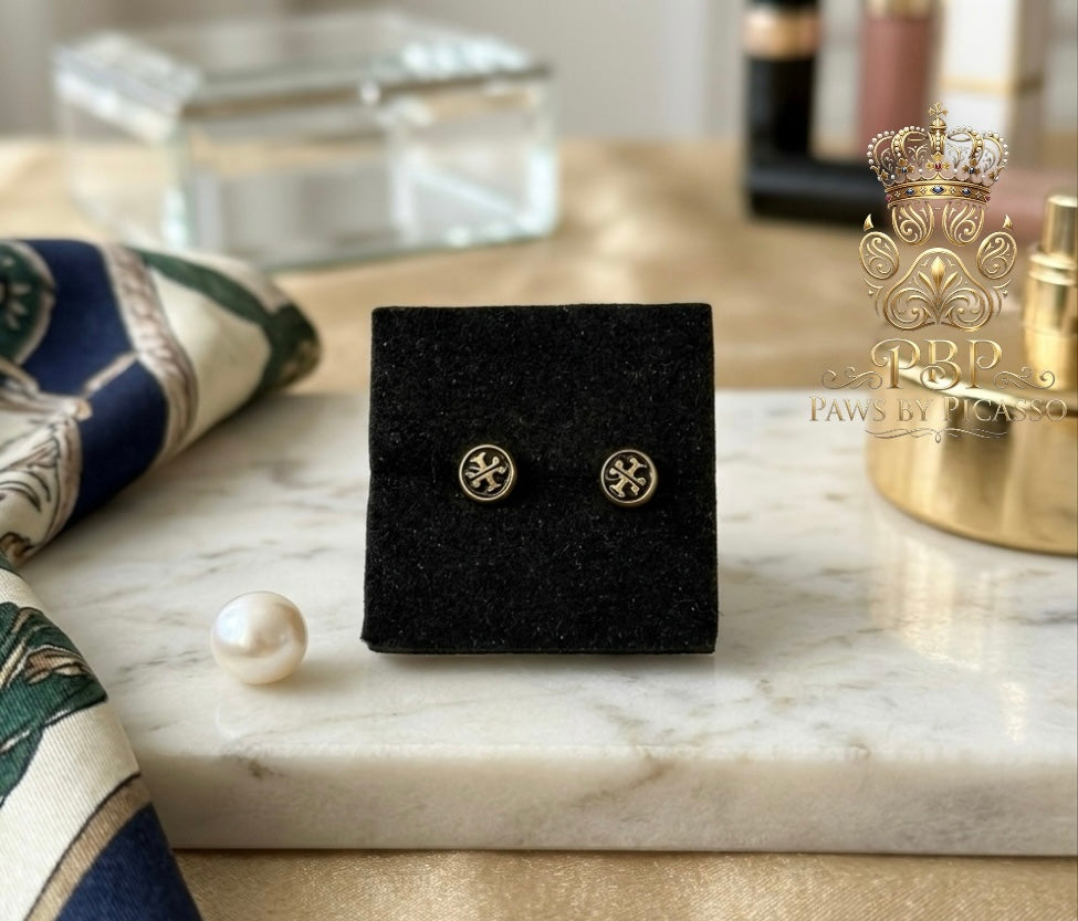 Gold earrings on a black display box with a pearl on a marble surface, branded 'Paws by Picasso 
