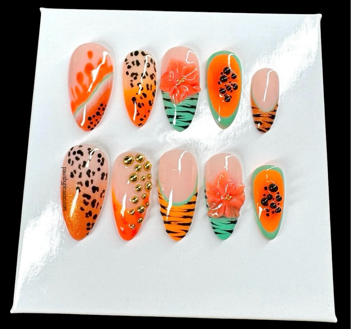 A set of ten decorative press-on nails displayed on a white backing card against a black background. The nails feature tropical and animal-inspired designs including orange gradients, leopard prints, floral motifs, and tiger stripes.